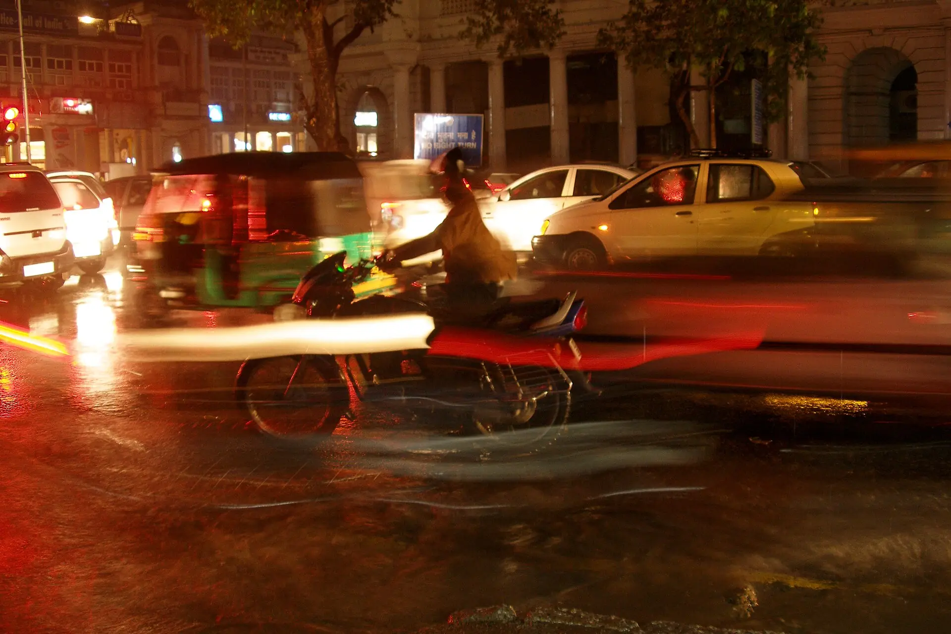 A two-wheeler rider in evening traffic on a wet street in Delhi